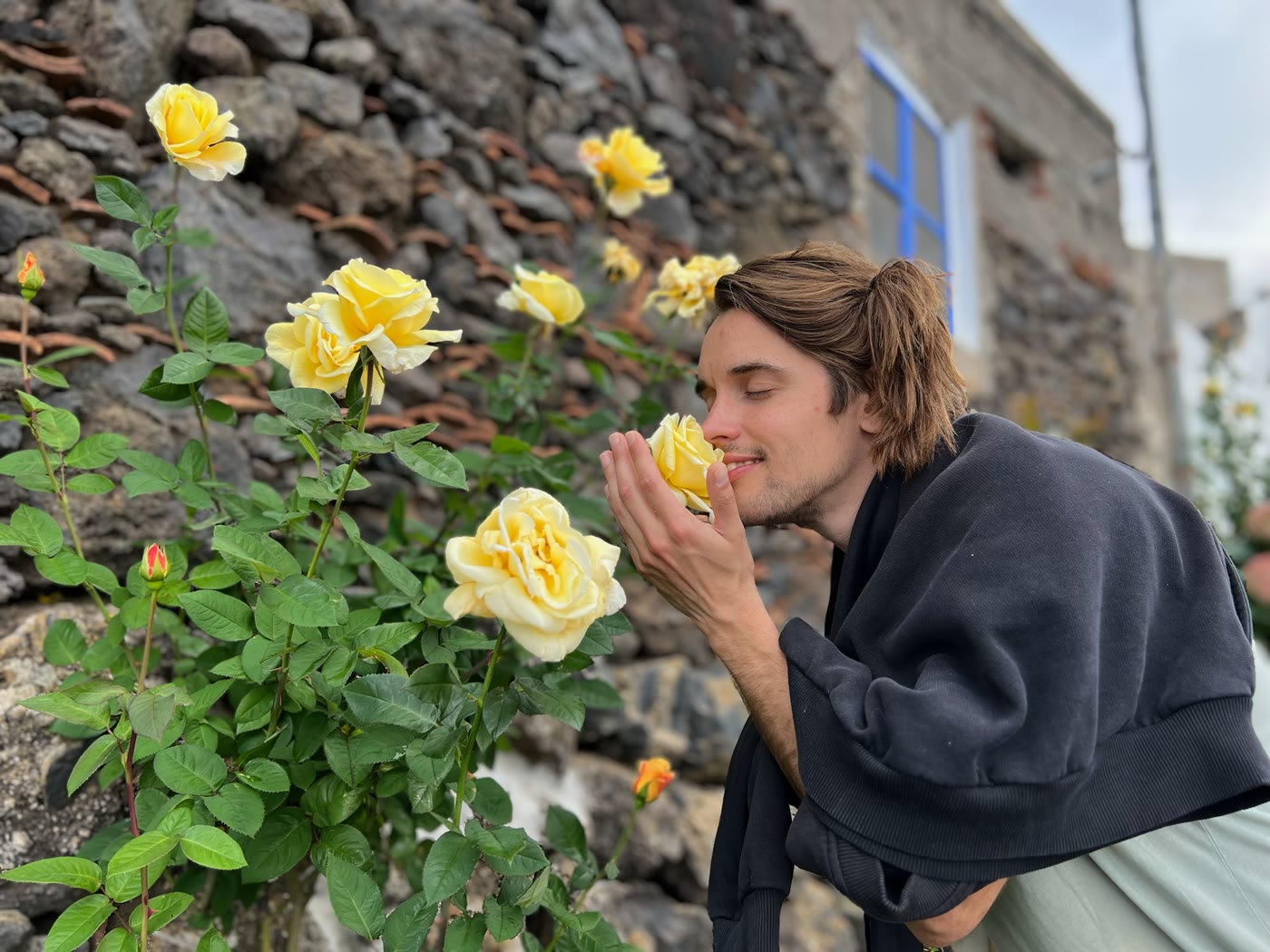 Joris Skudra, Lithuanian documentary director, smelling a yellow rose by a stone wall