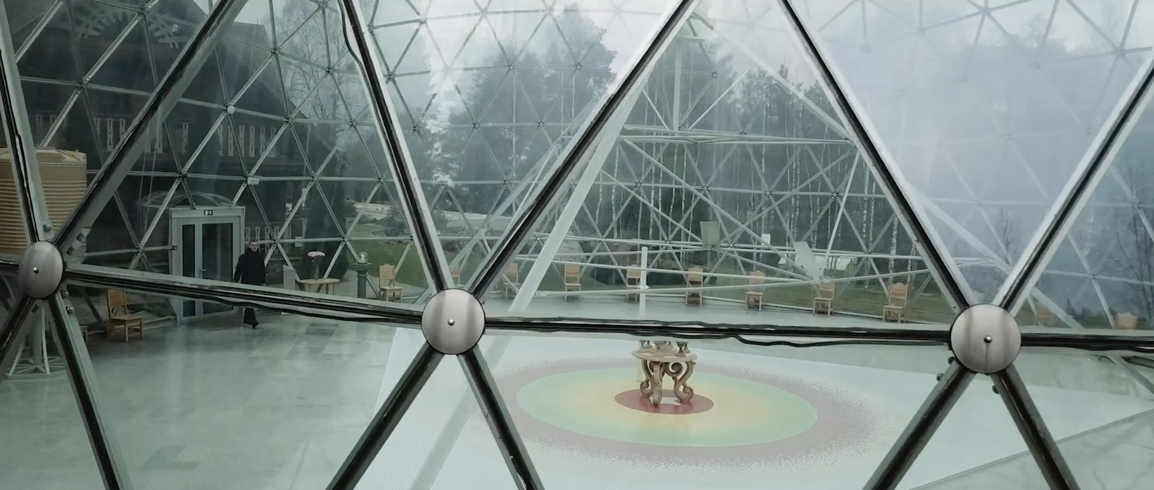 Inside the geodesic glass dome with a mosaic floor and wooden chairs, The Dome