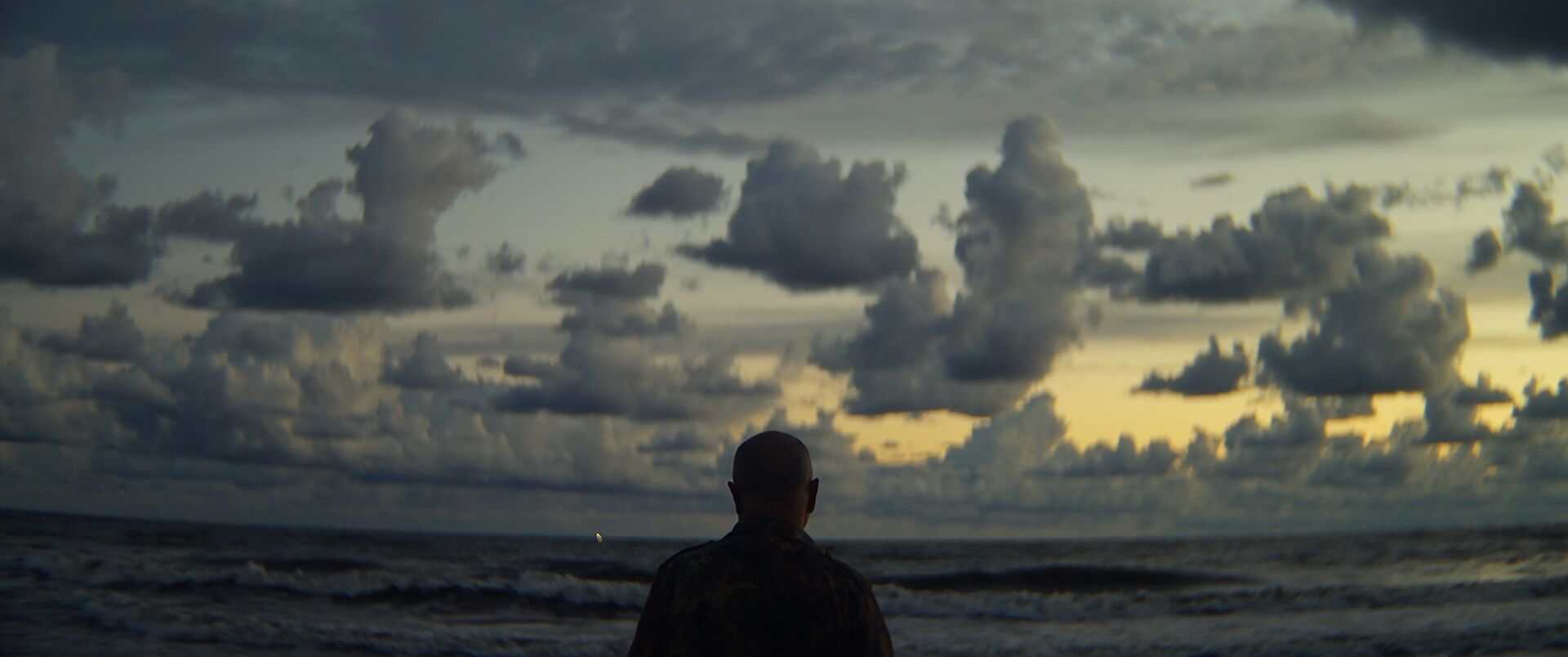 Romualdas Požerskis silhouetted by the sea under storm clouds, Under the Red Light