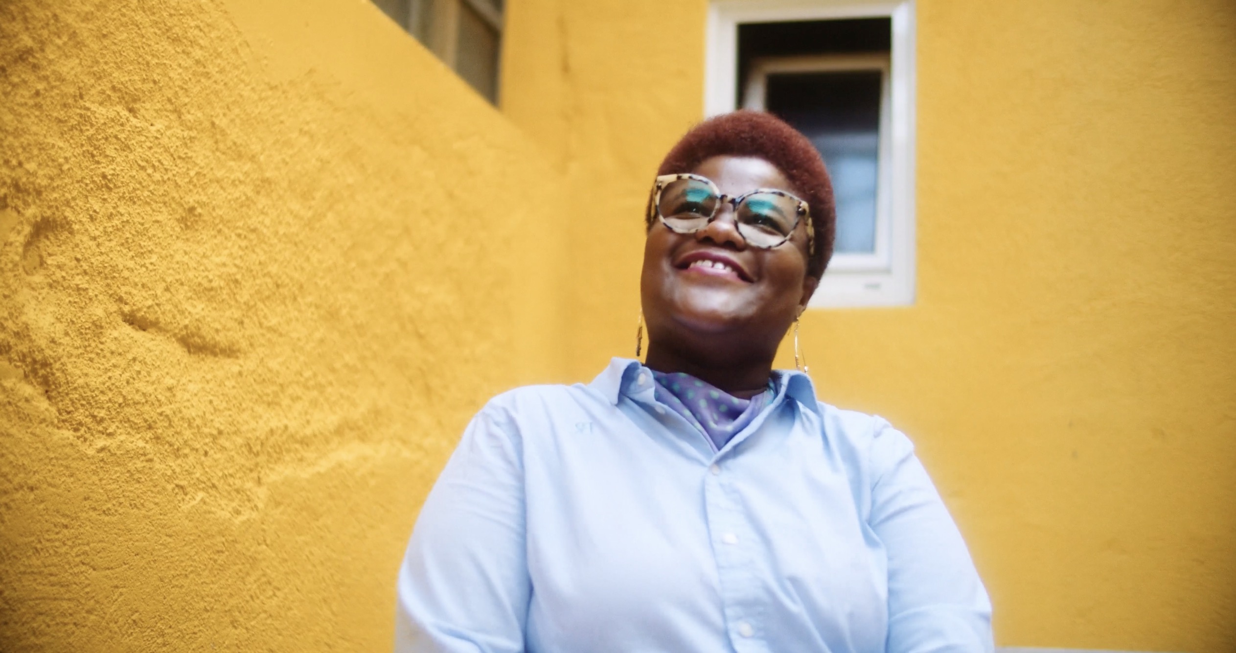 A smiling woman in front of a yellow wall, Women in Tech for CodeOp